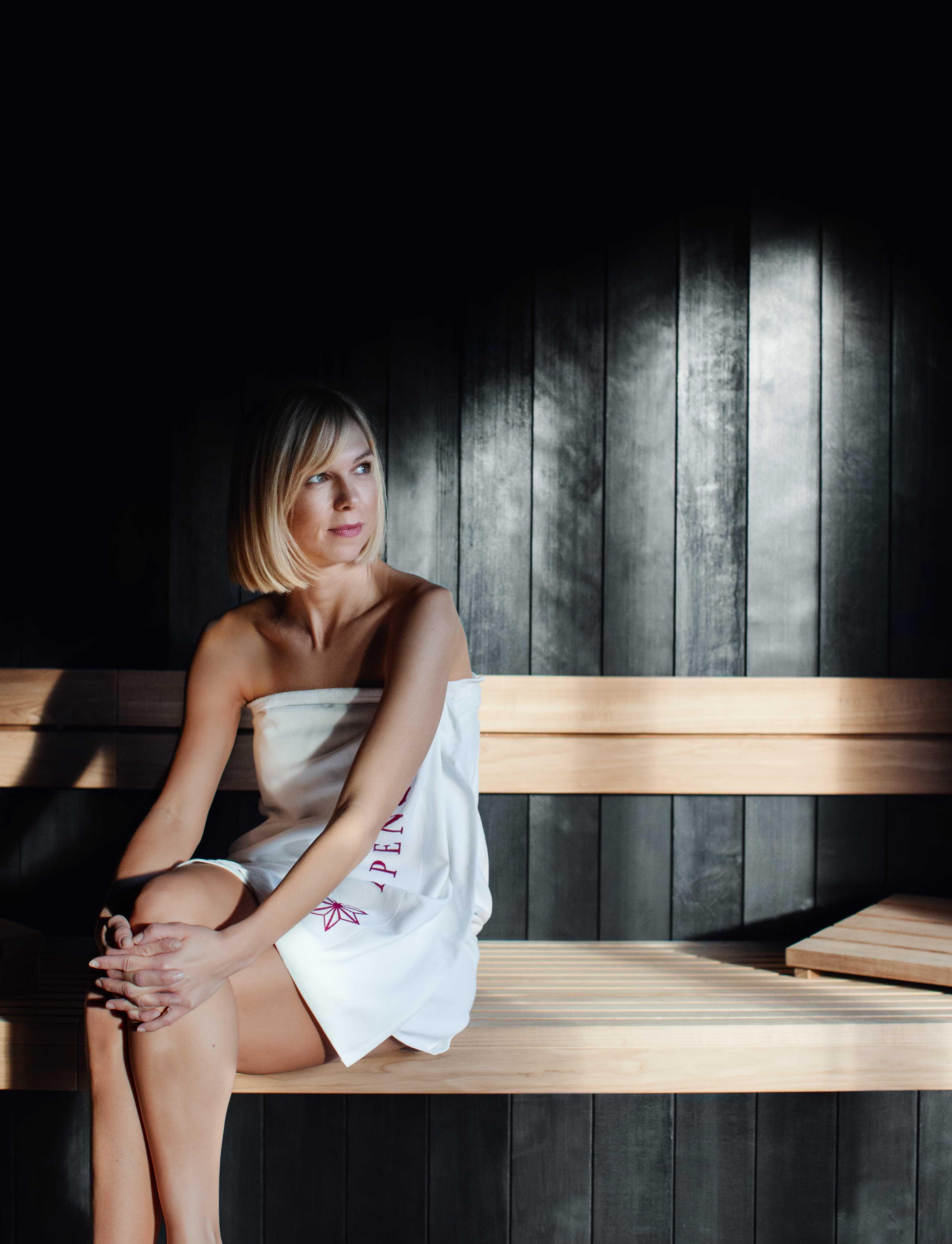 full body shot of a woman in a sauna, dressed with a towel.