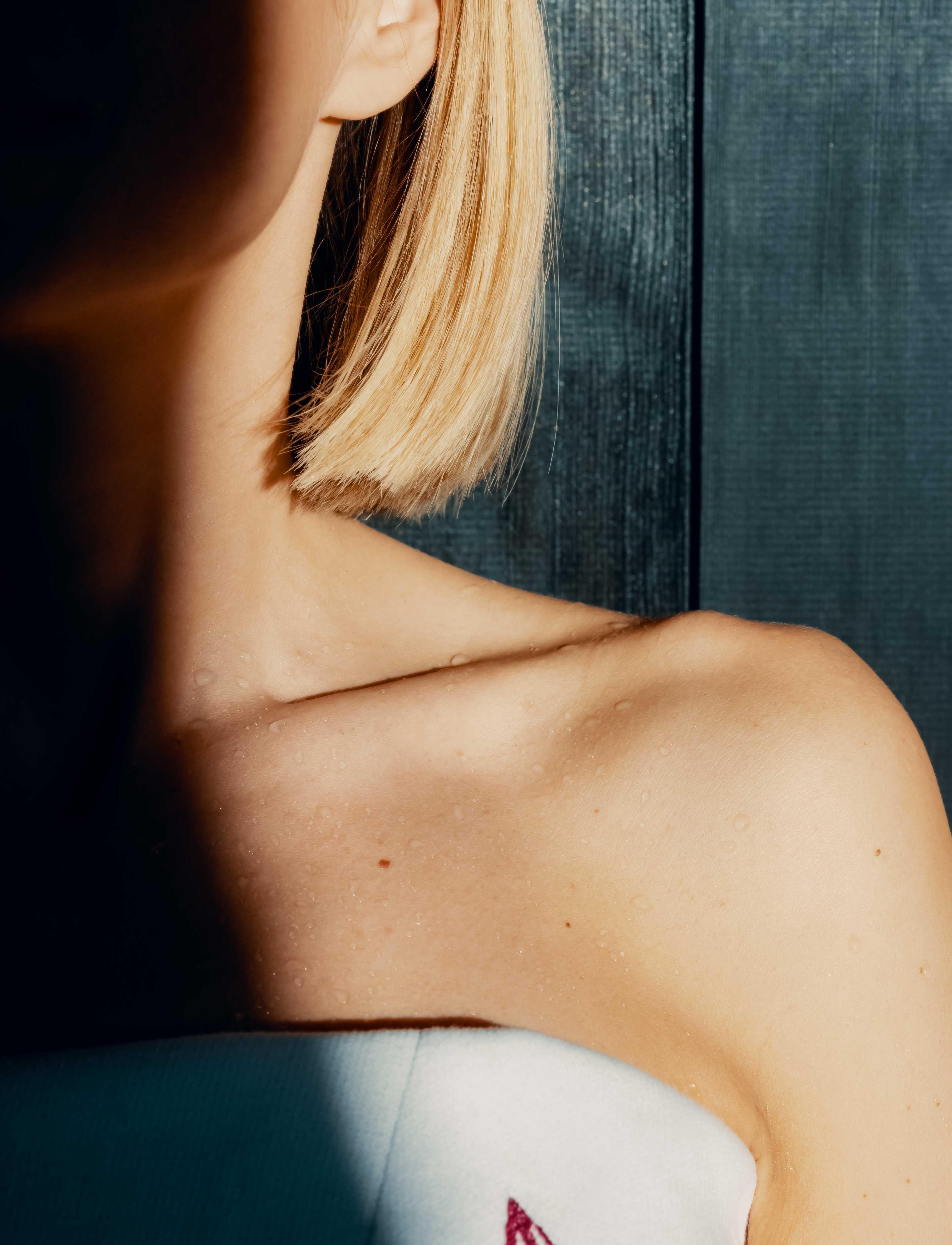 detail of the shoulder of a woman sitting in the sauna with beads of sweat on her skin.