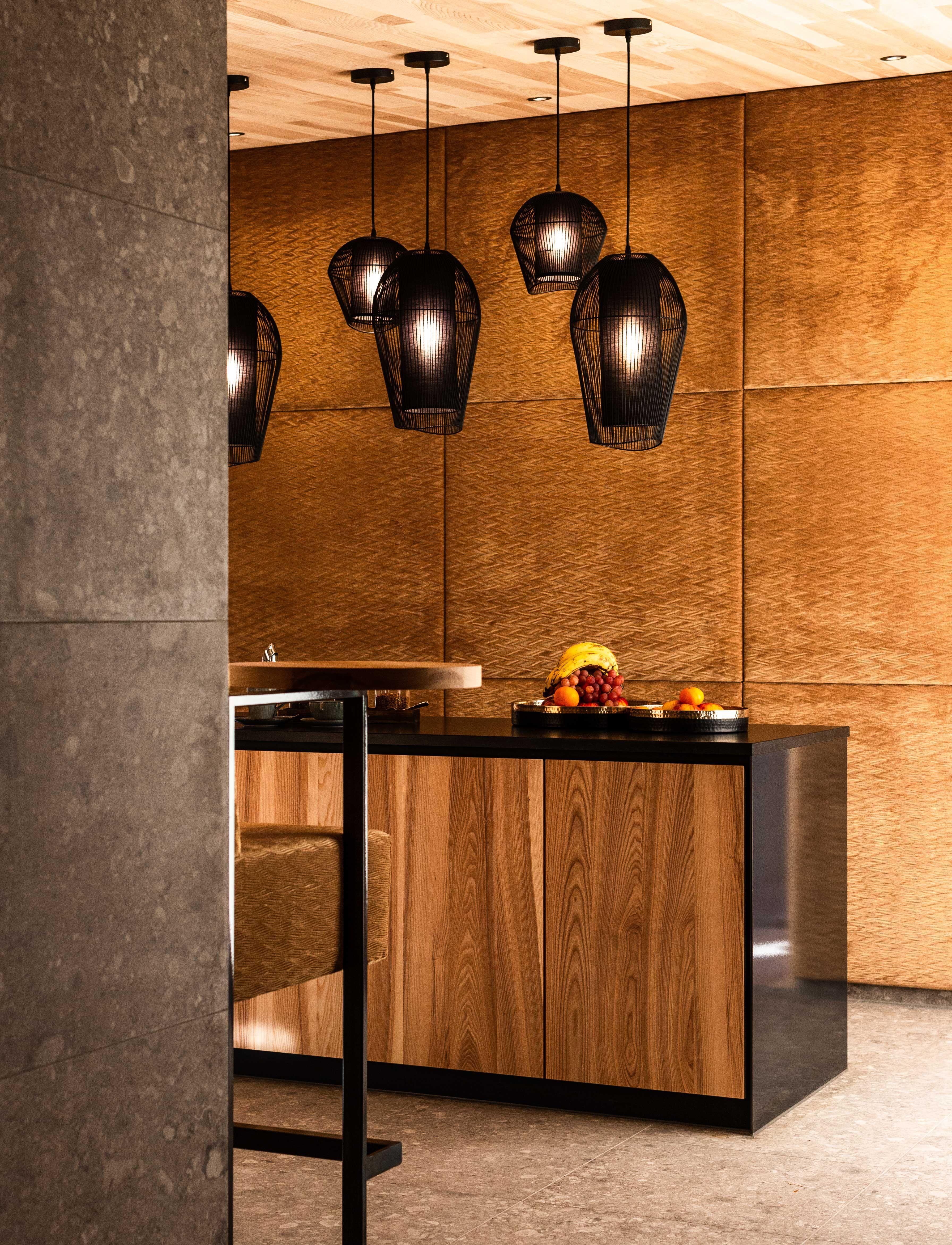 shot of a sideboard with a bowl of fruits in front of a wall which is wallpapered with golden fabric. 