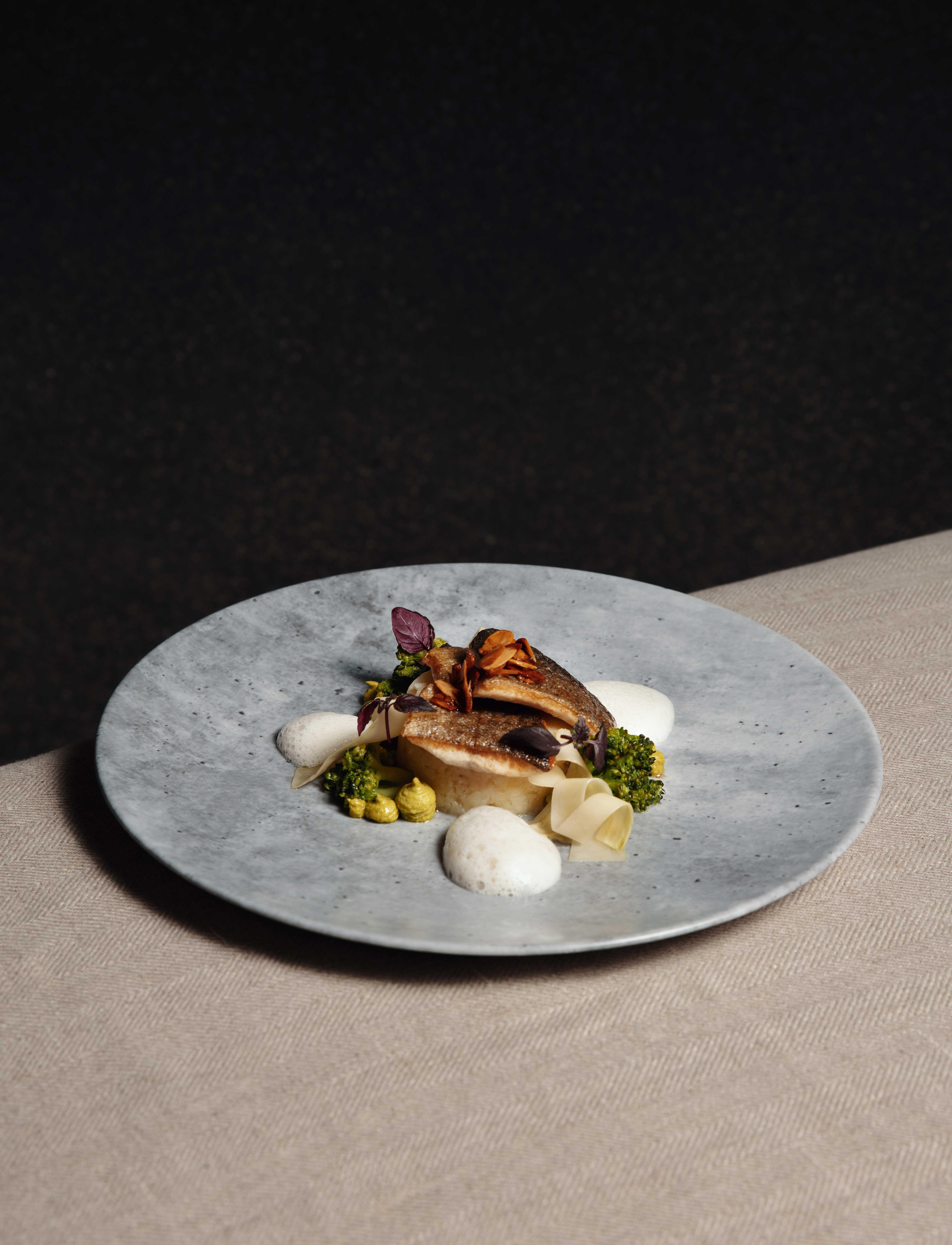 gray plate with a fish dish on a linen background and in front of a black wall.