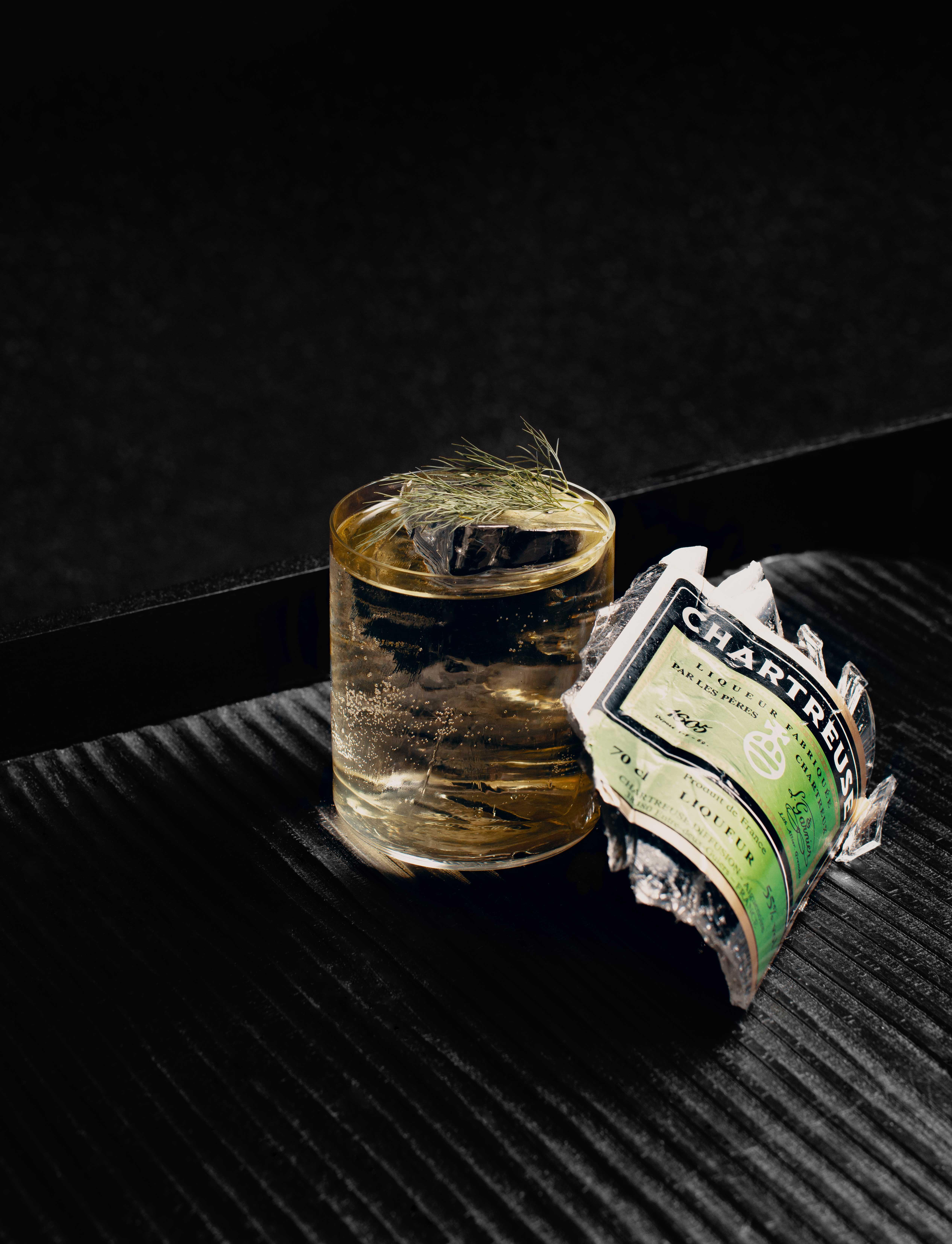 a transparent cocktail in a black room with a piece of a broken bottle.