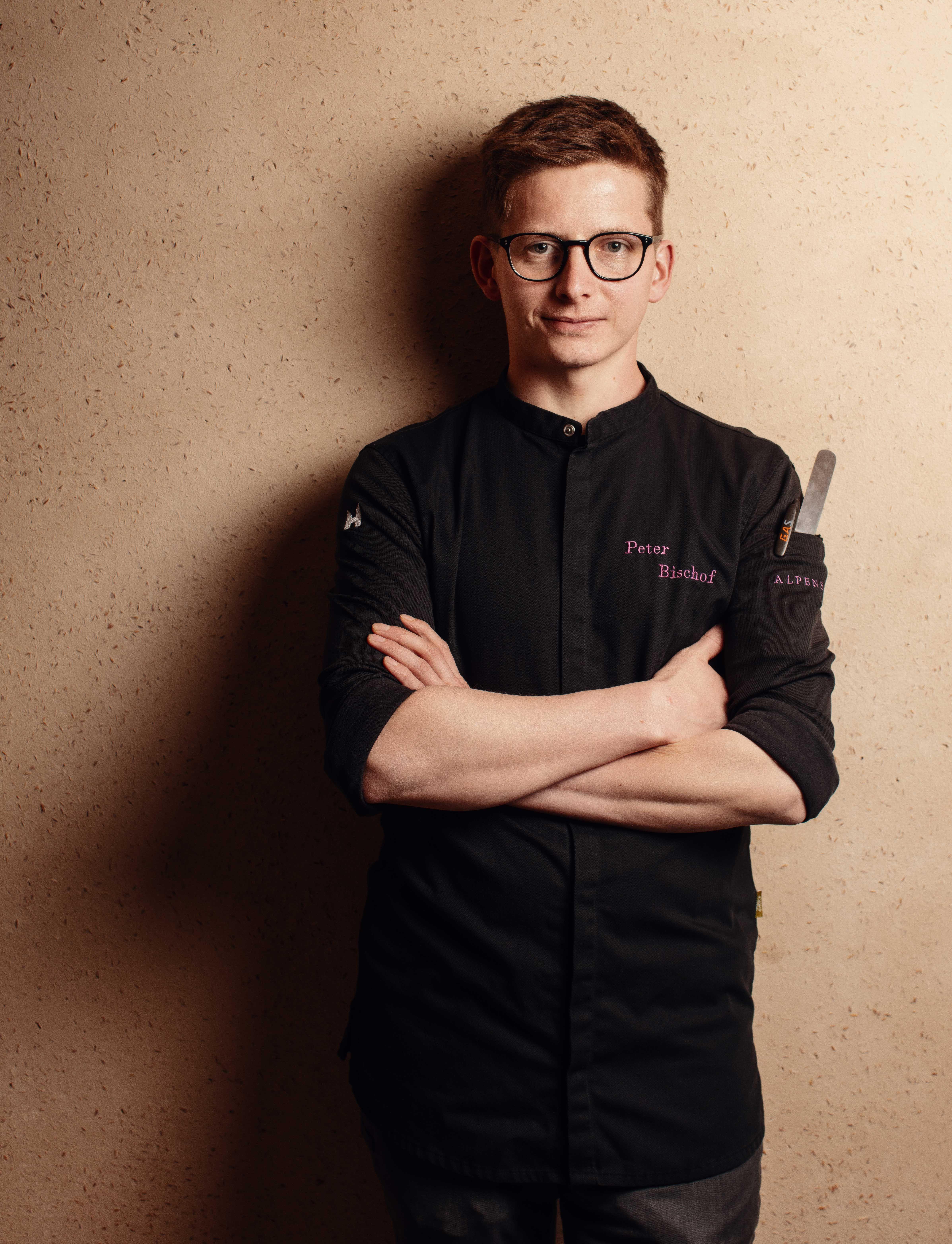 portrait of a young cook in work clothes in front of a golden wall.