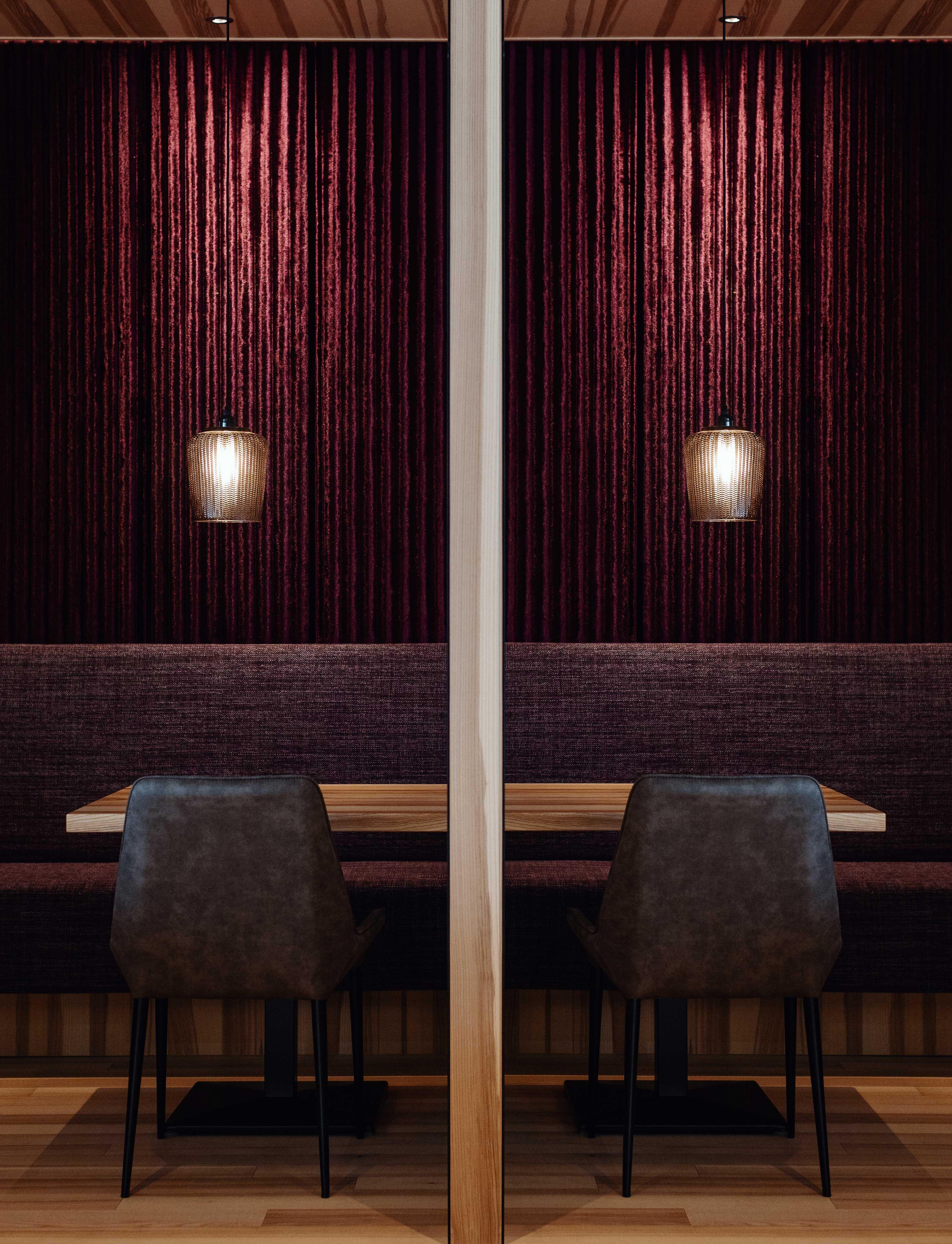 interior design shot of a restaurant, you see a table with two chairs and two lamps hanging over it in front of a velvet covered purple wall.