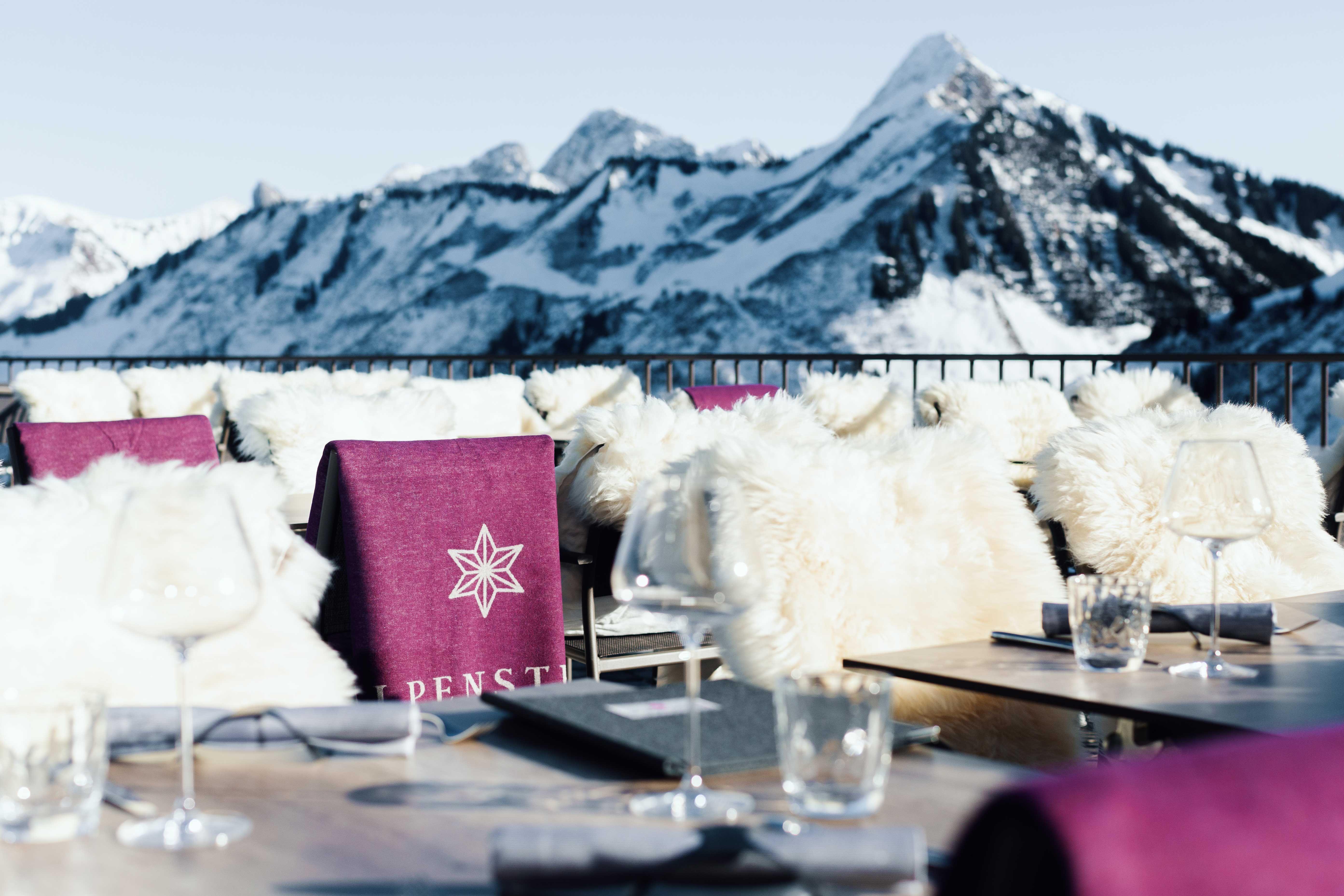 detail of a roof terrace in winter, in the background the snowy mountain landscape, in the foreground some covered outdoor tables and chairs white fur. 