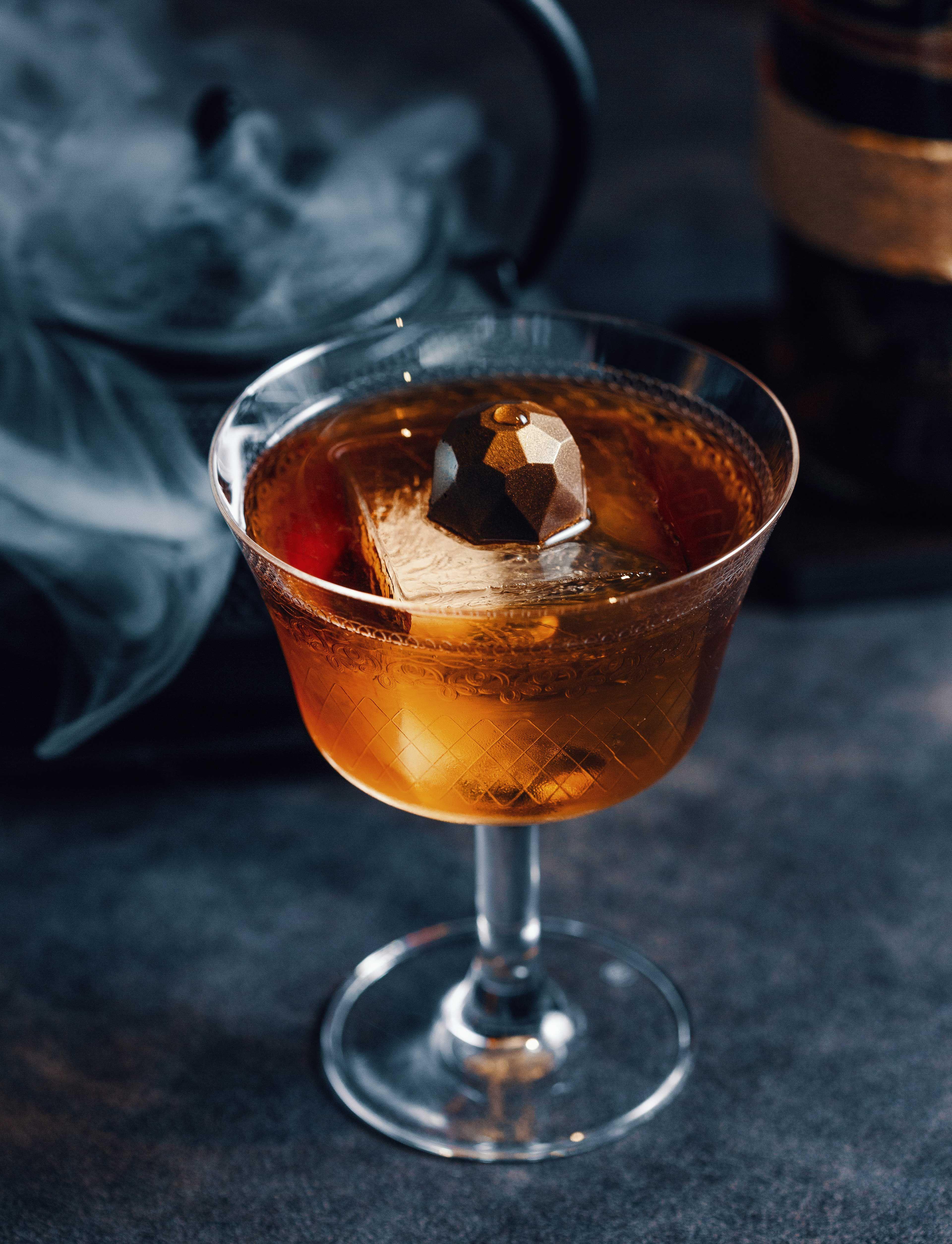 a filled cocktail glass with an ice cube in it. on the ice cube is a chocolate praline.