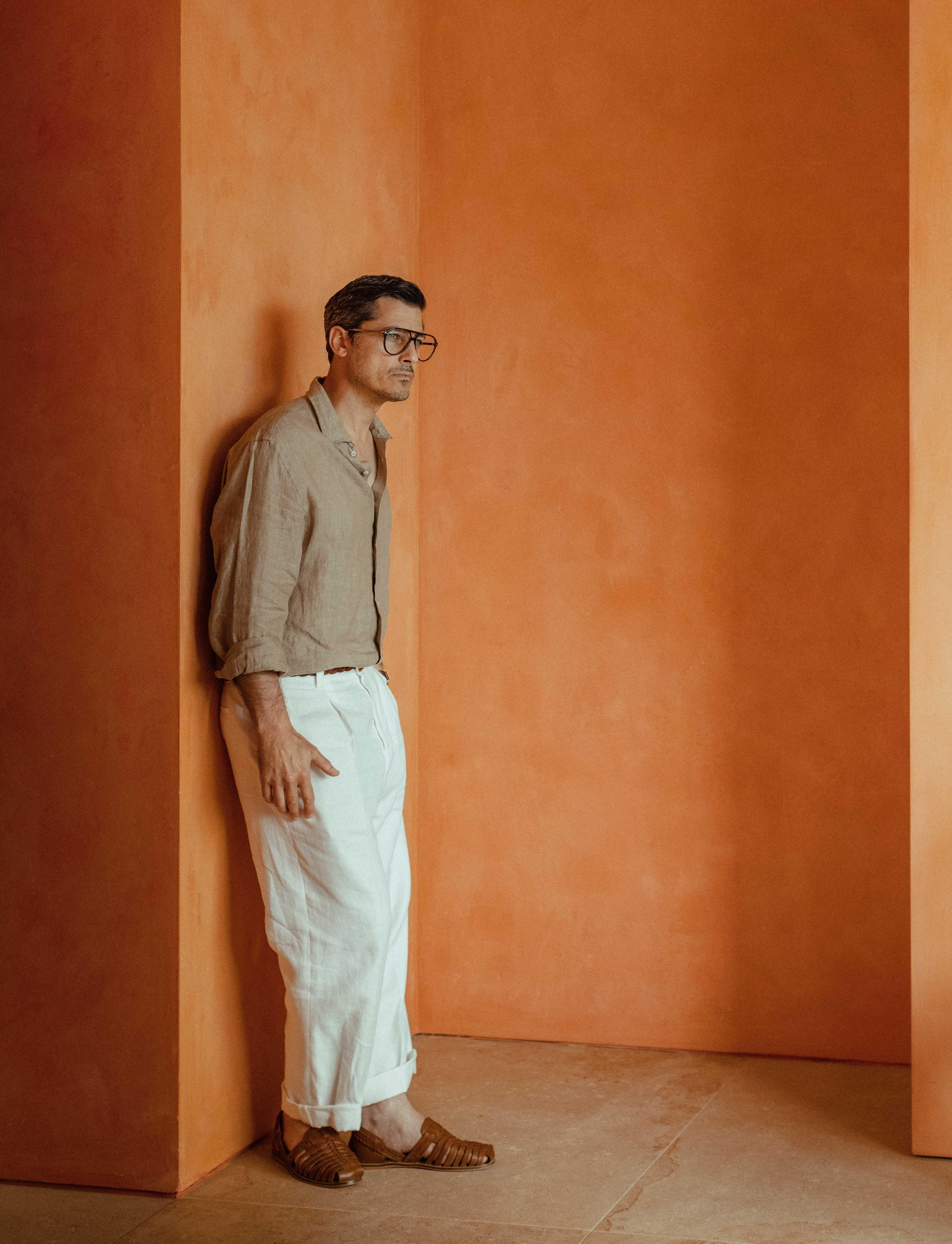 man with dark hair and optical glasses stands in a small room with orange walls.