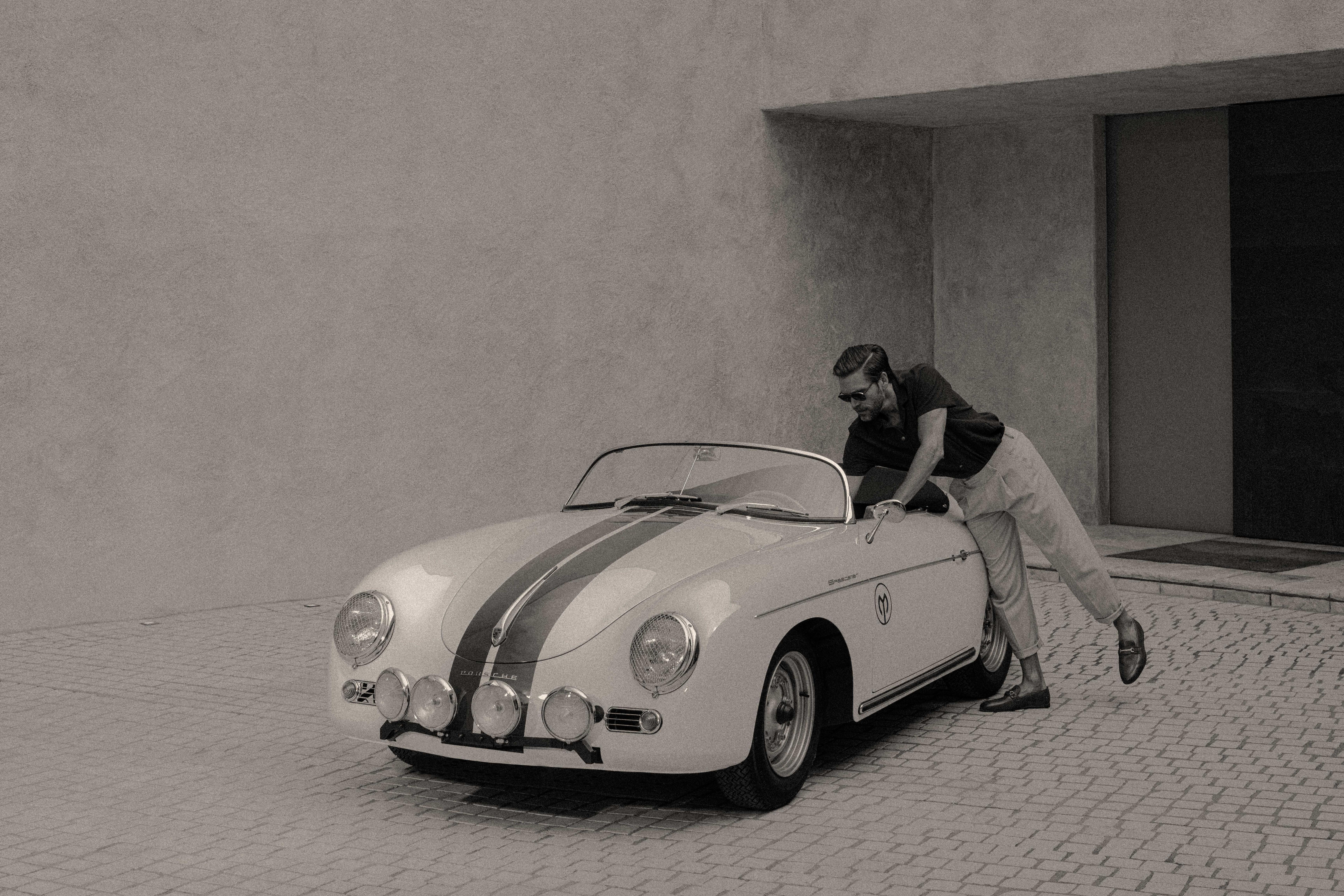 photograph of a man in front of a house with a vintage porsche.