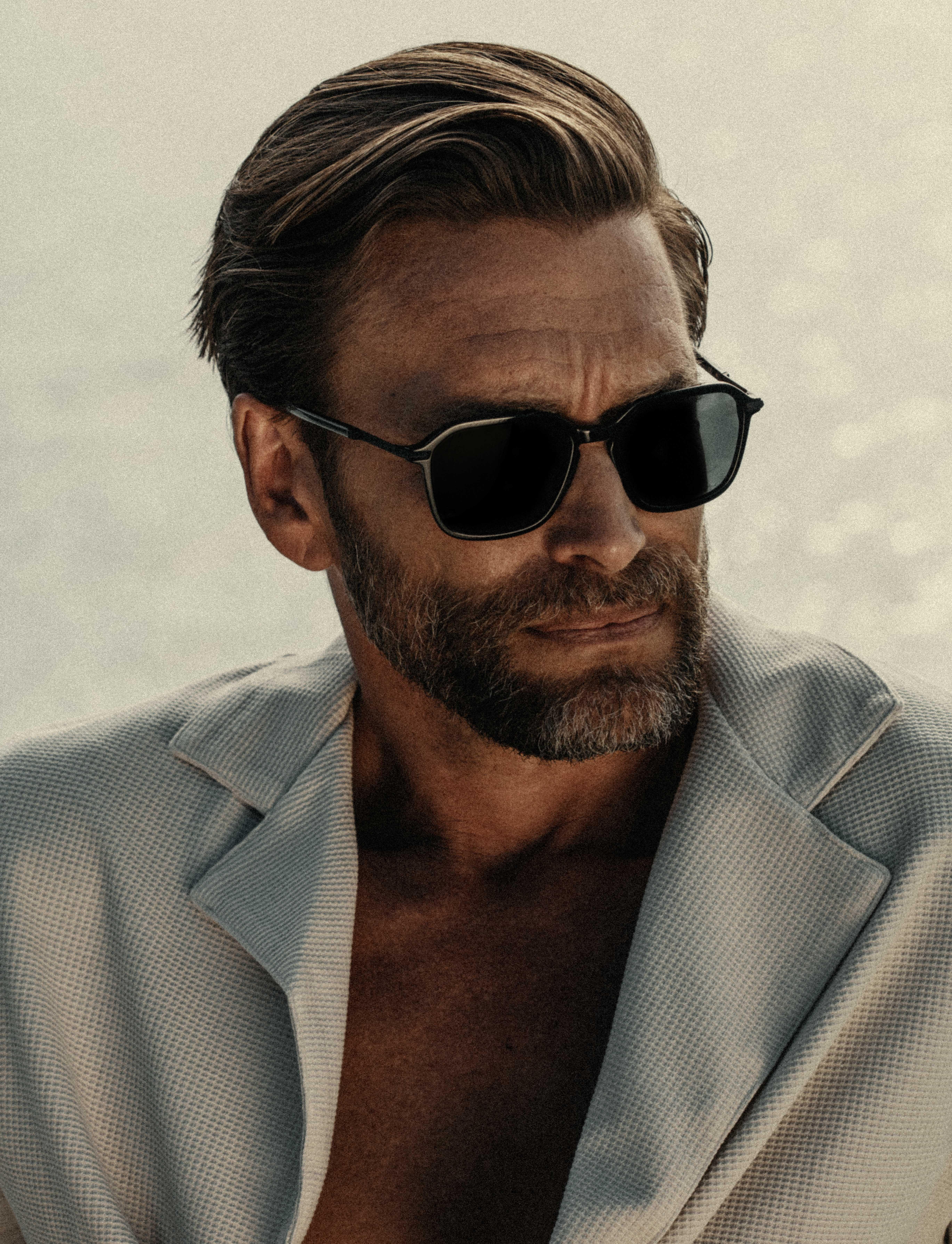 portrait of a man with linen shirt and black sunglasses, in the background you can see only water.