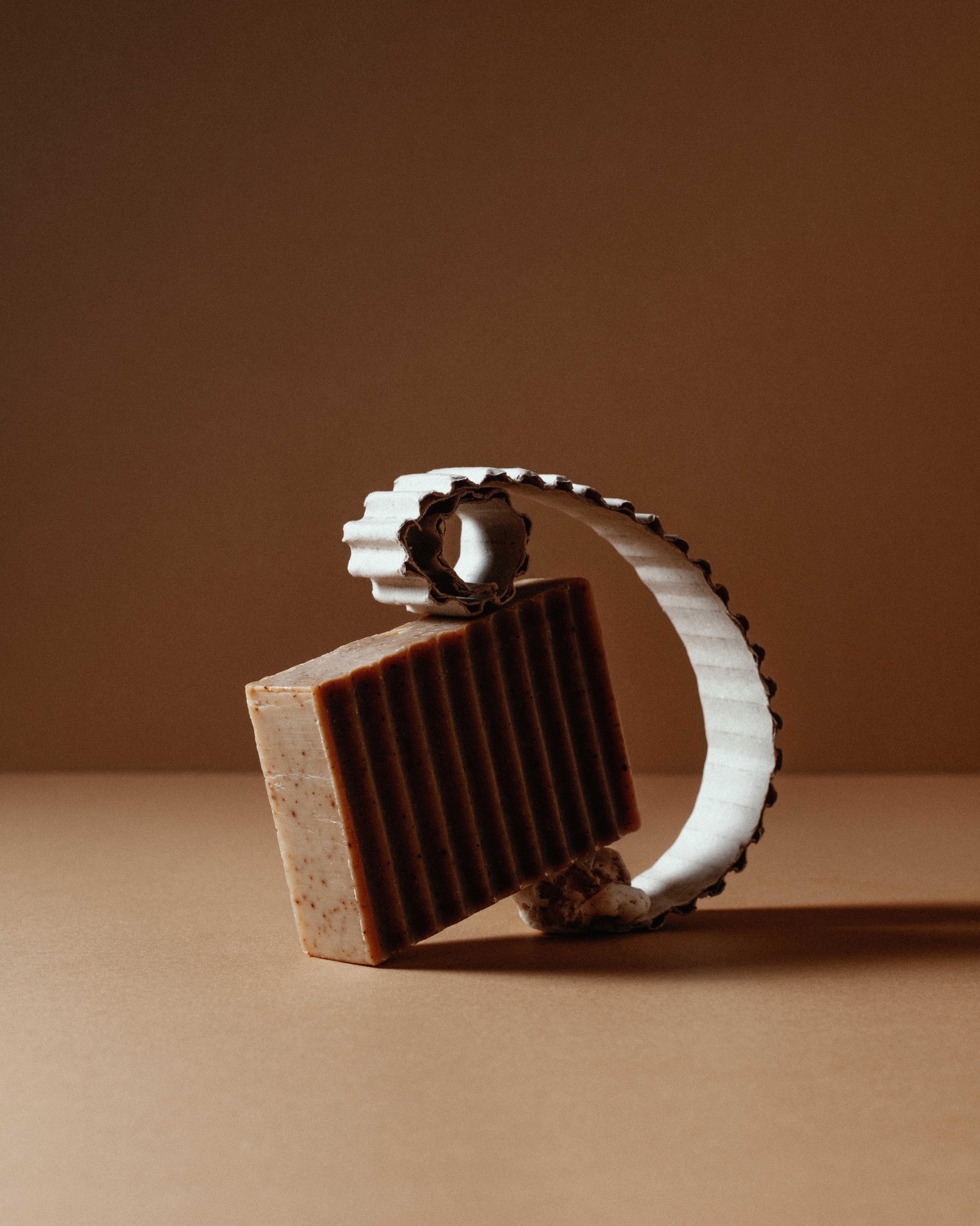  photo of a soap with grooves and a cardboard strip also grooved against brown background.