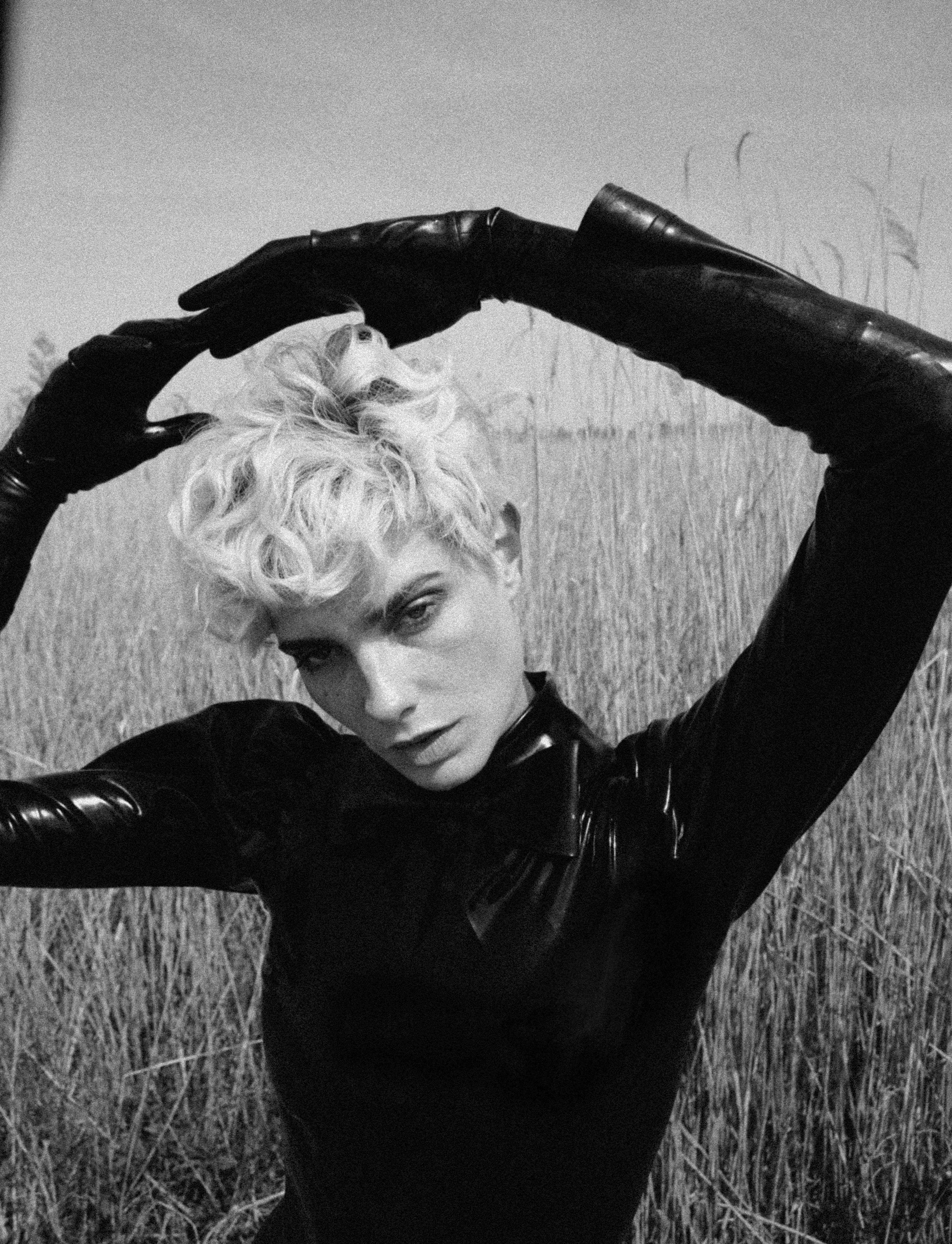 a young woman stands in the middle of a wheat field and brings her arms and hands together above her head. 