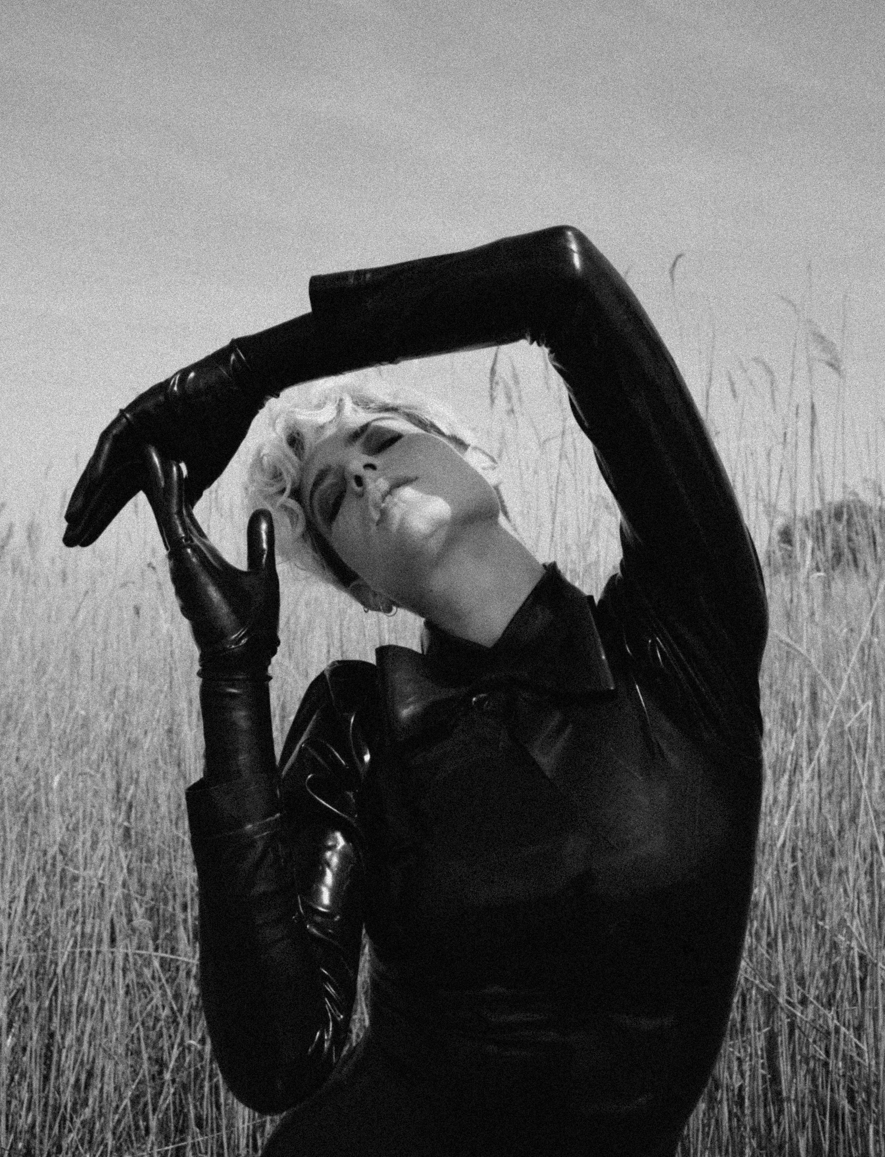 a young woman stands in the middle of a wheat field and brings her arms and hands together above her head. 