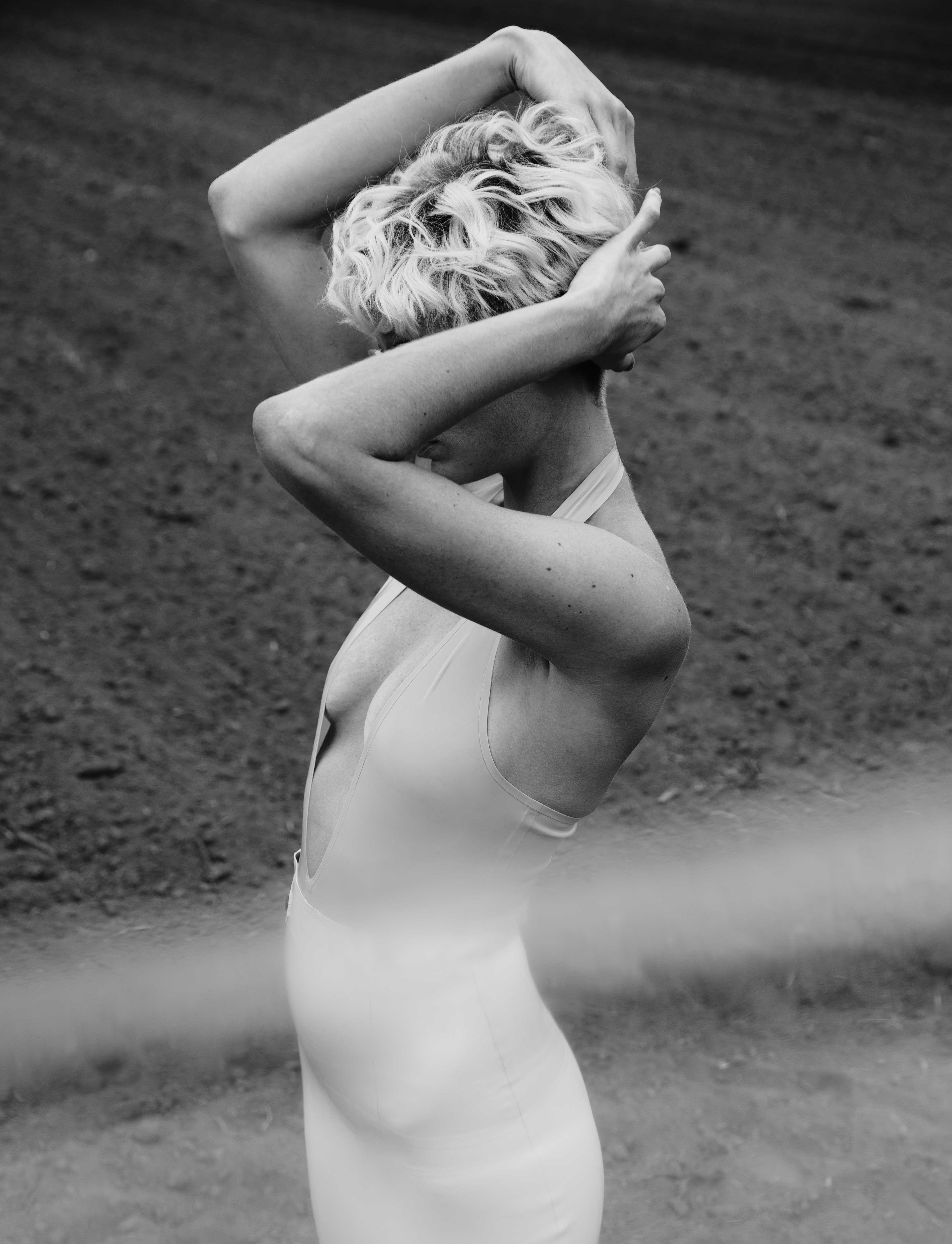 a young woman stands in tight latex clothes on a field and holds her hands in front of her face.