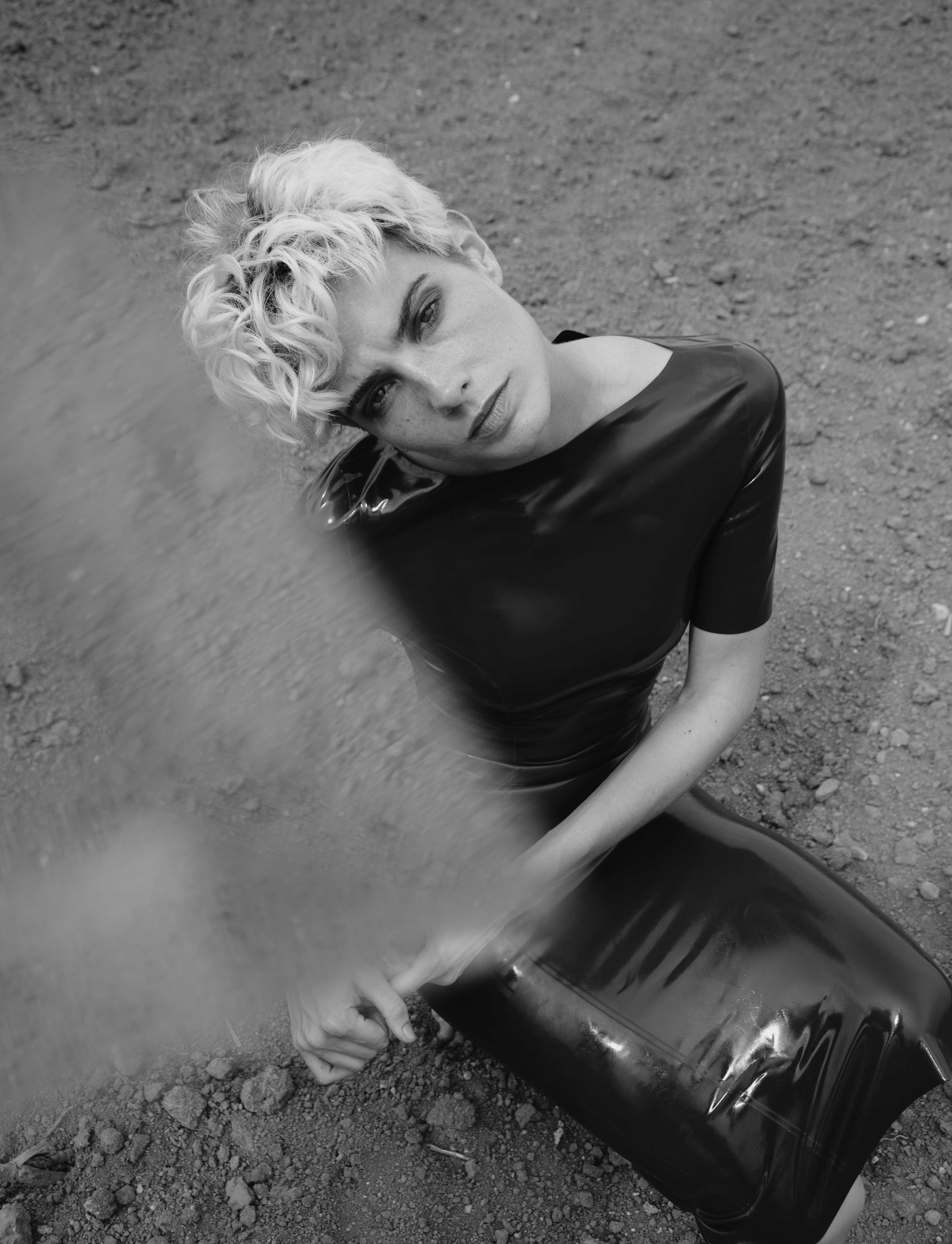 a woman sits in a tight latex dress at the bottom of a field.