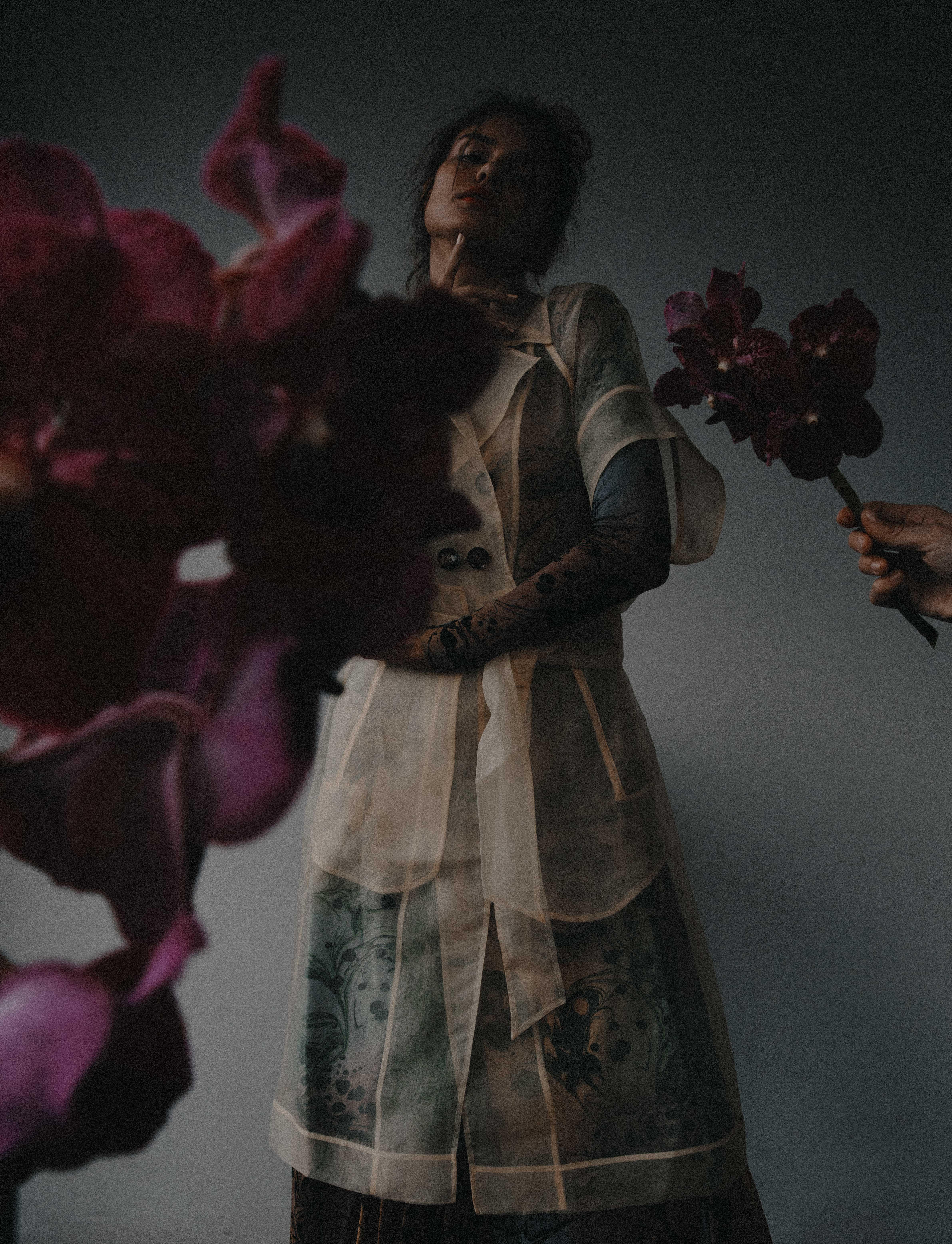 portrait of woman in a dress with purple orchids in the foreground.