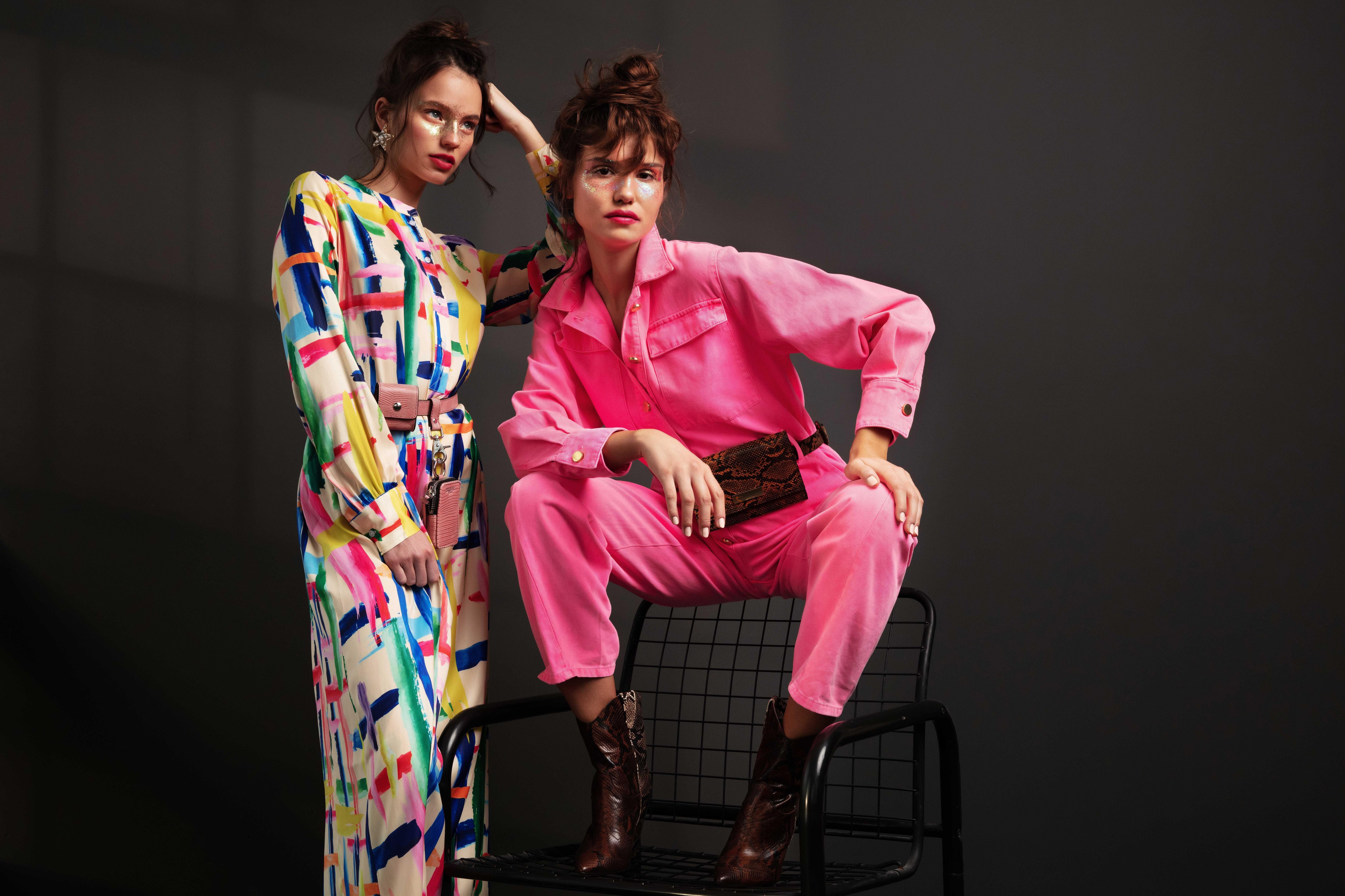 portrait of two women, one with pink jumpsuit one with colorful dress.