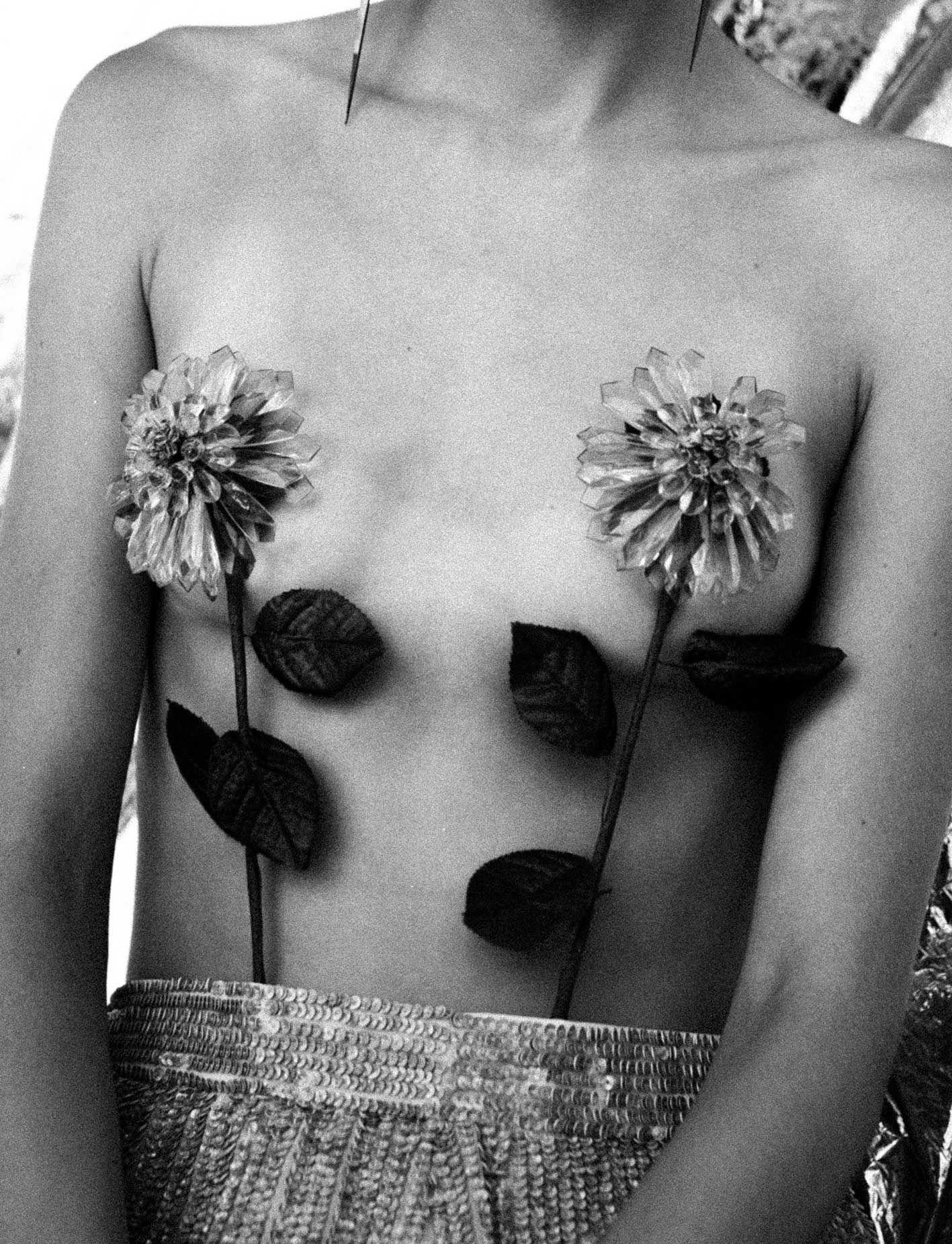 closeup of a female torso with glass flowers over her breasts.