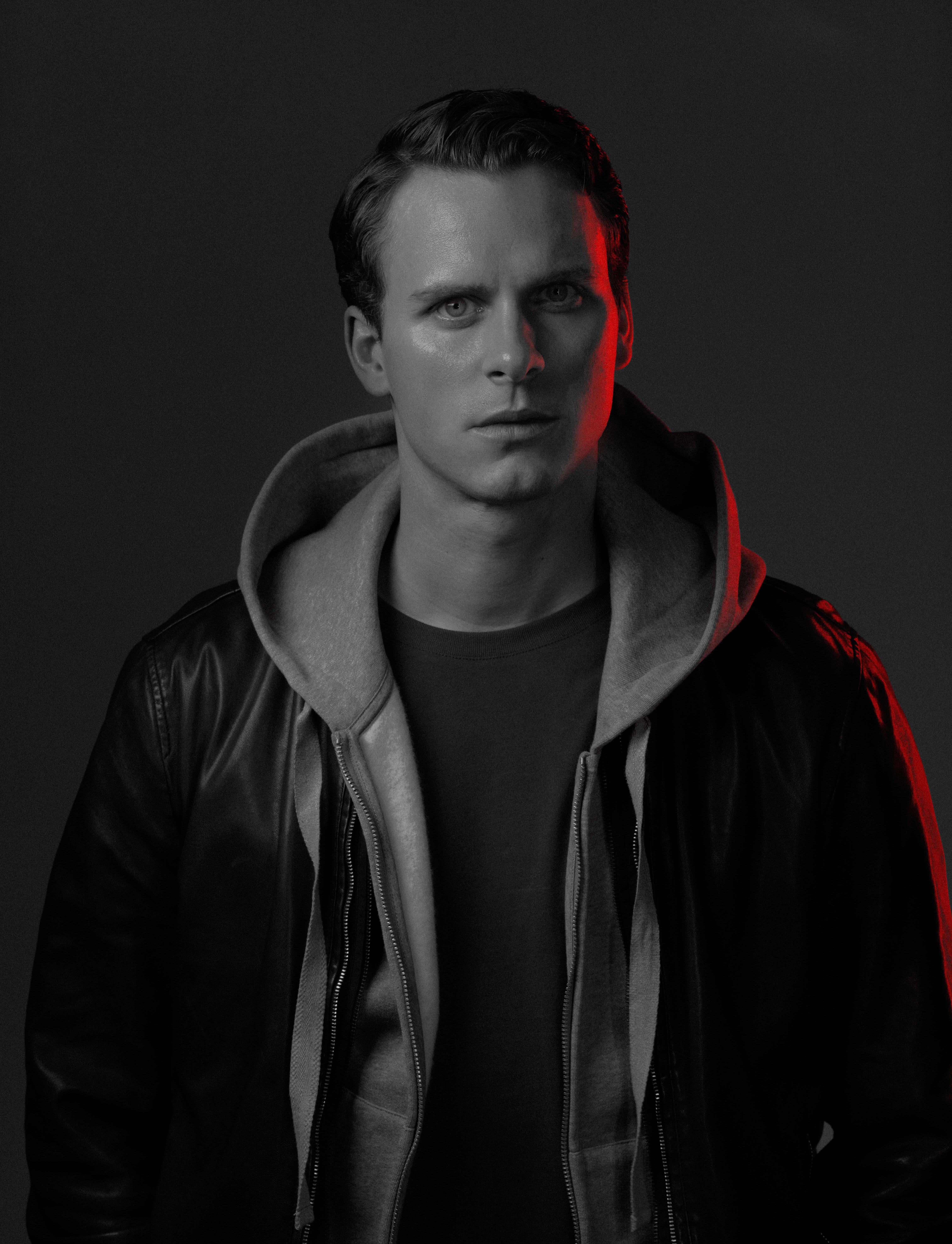 black and white photo of a young actor in a black leather jacket looks at us. half of his face is illuminated in red.