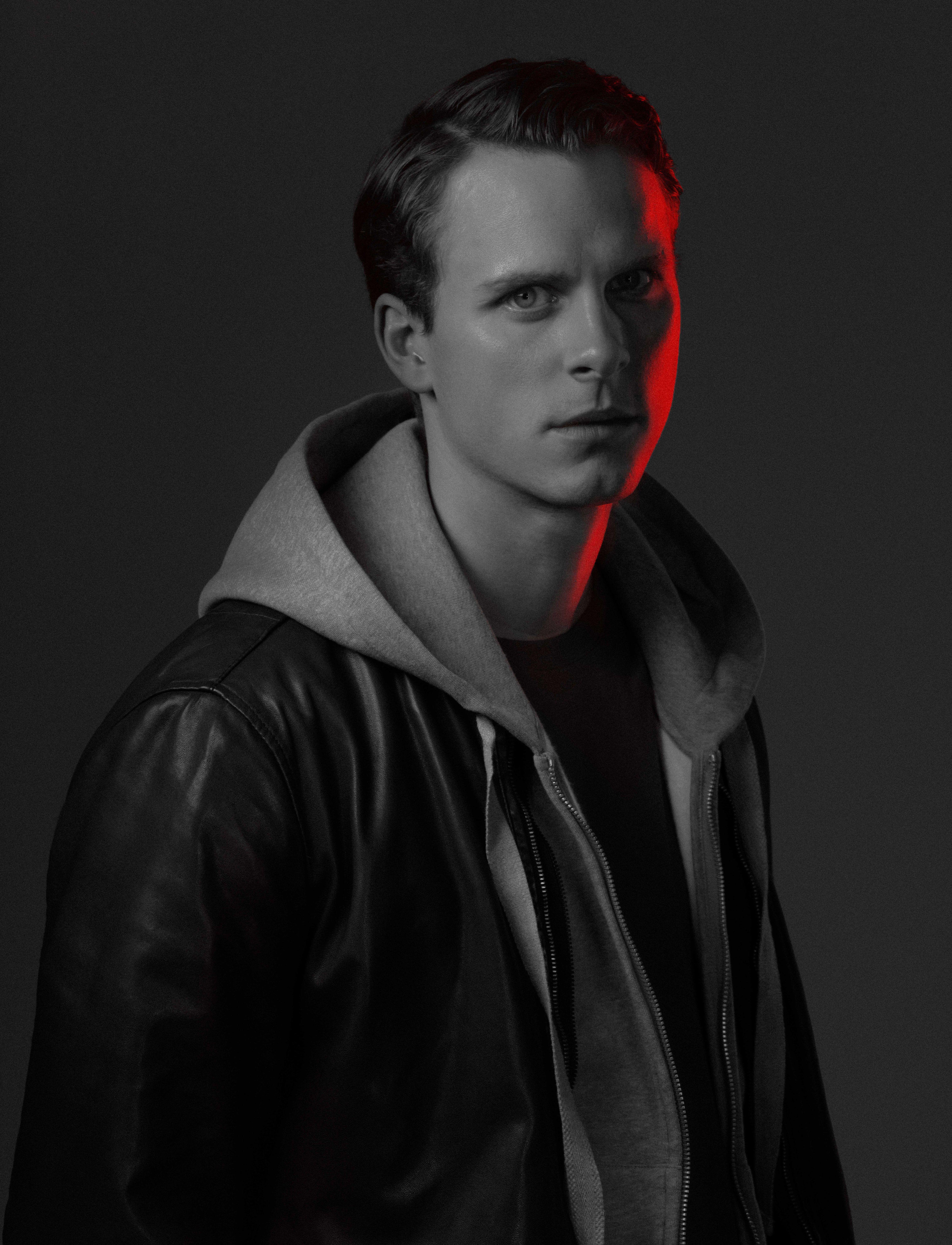 black and white photo of a young actor in a black leather jacket looks at us. half of his face is illuminated in red.