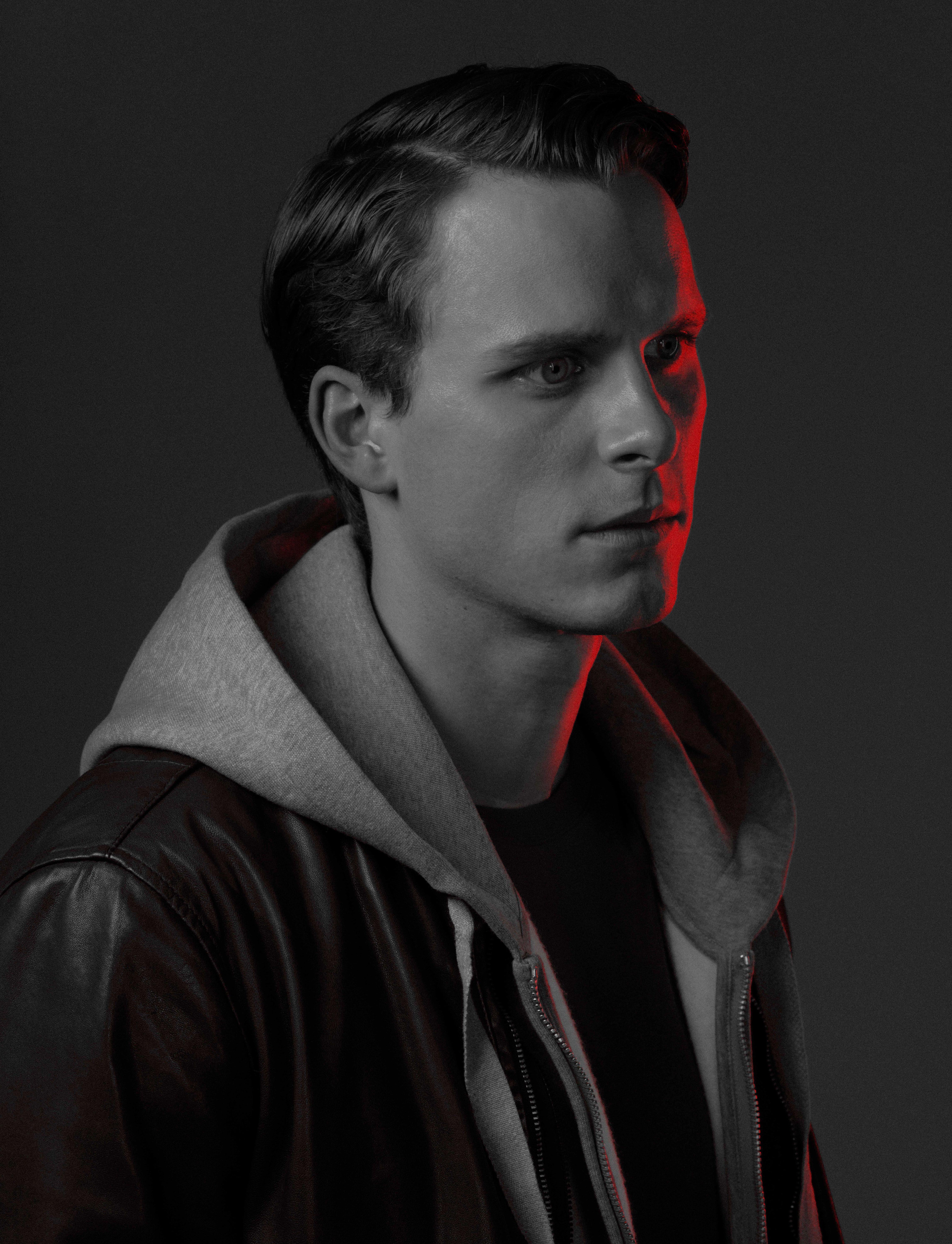 black and white photo of a young actor in a black leather jacket looks at us. half of his face is illuminated in red.