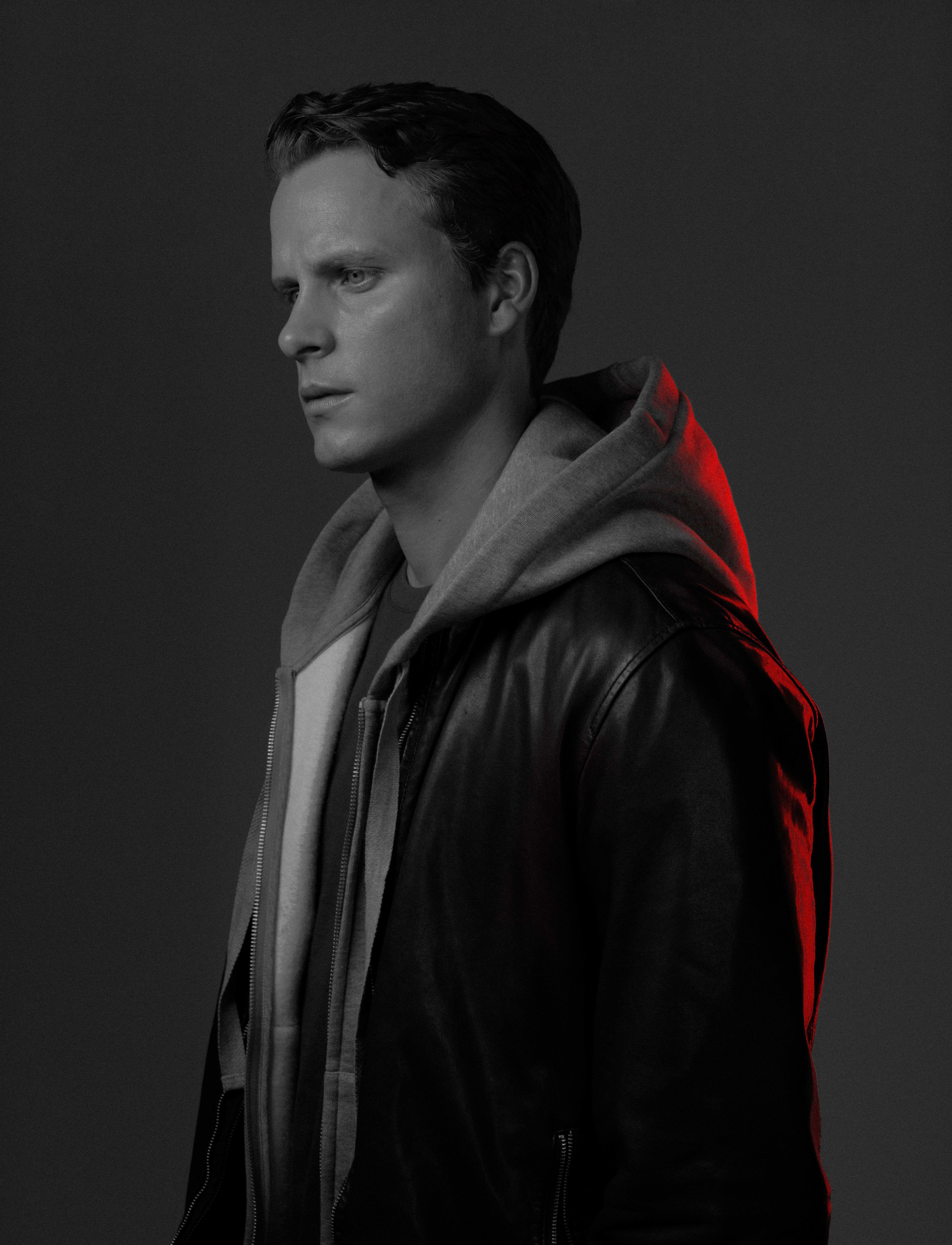 black and white photo of a young actor in a black leather jacket looks at us. half of his face is illuminated in red.