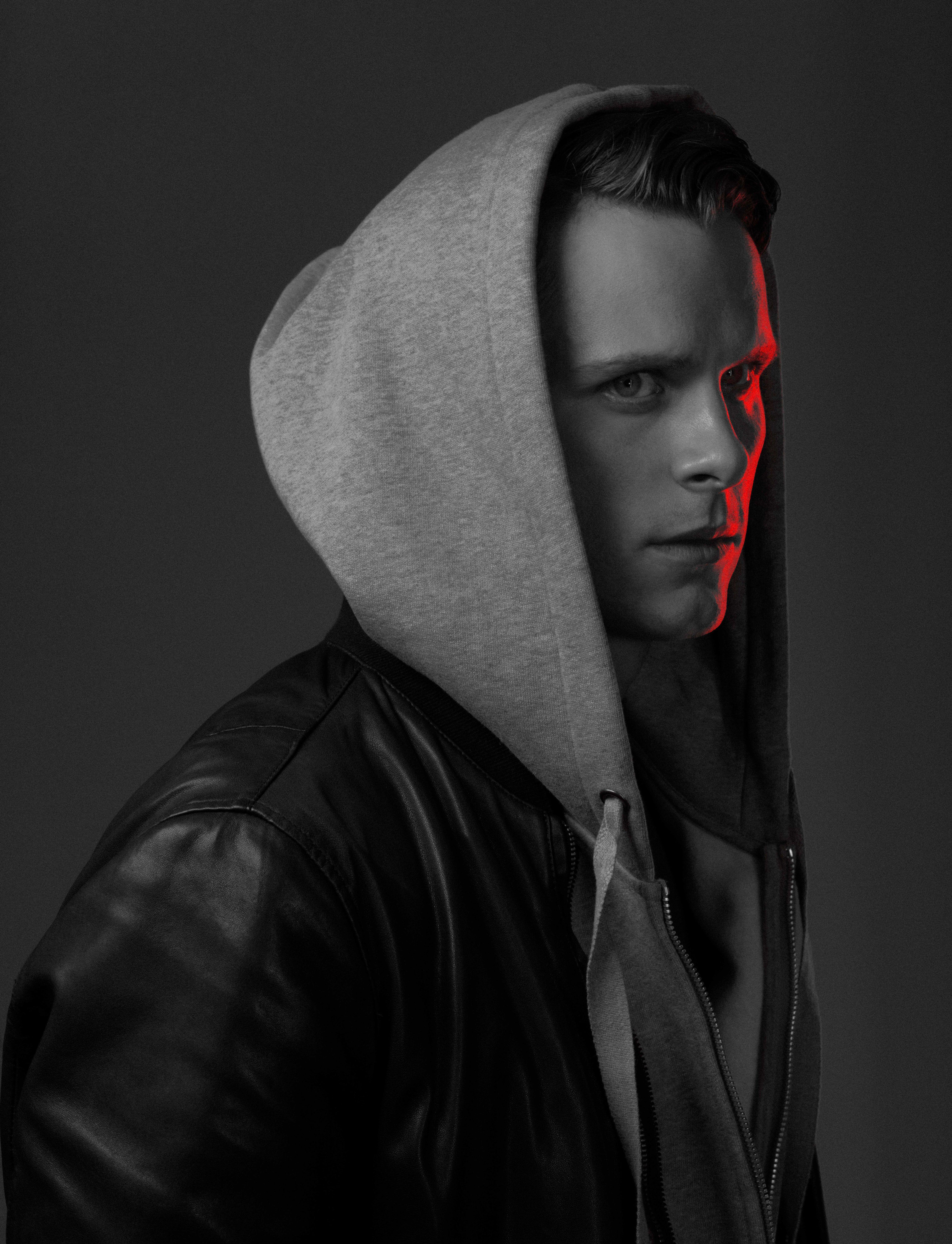 black and white photo of a young actor in a black leather jacket looks at us. half of his face is illuminated in red.