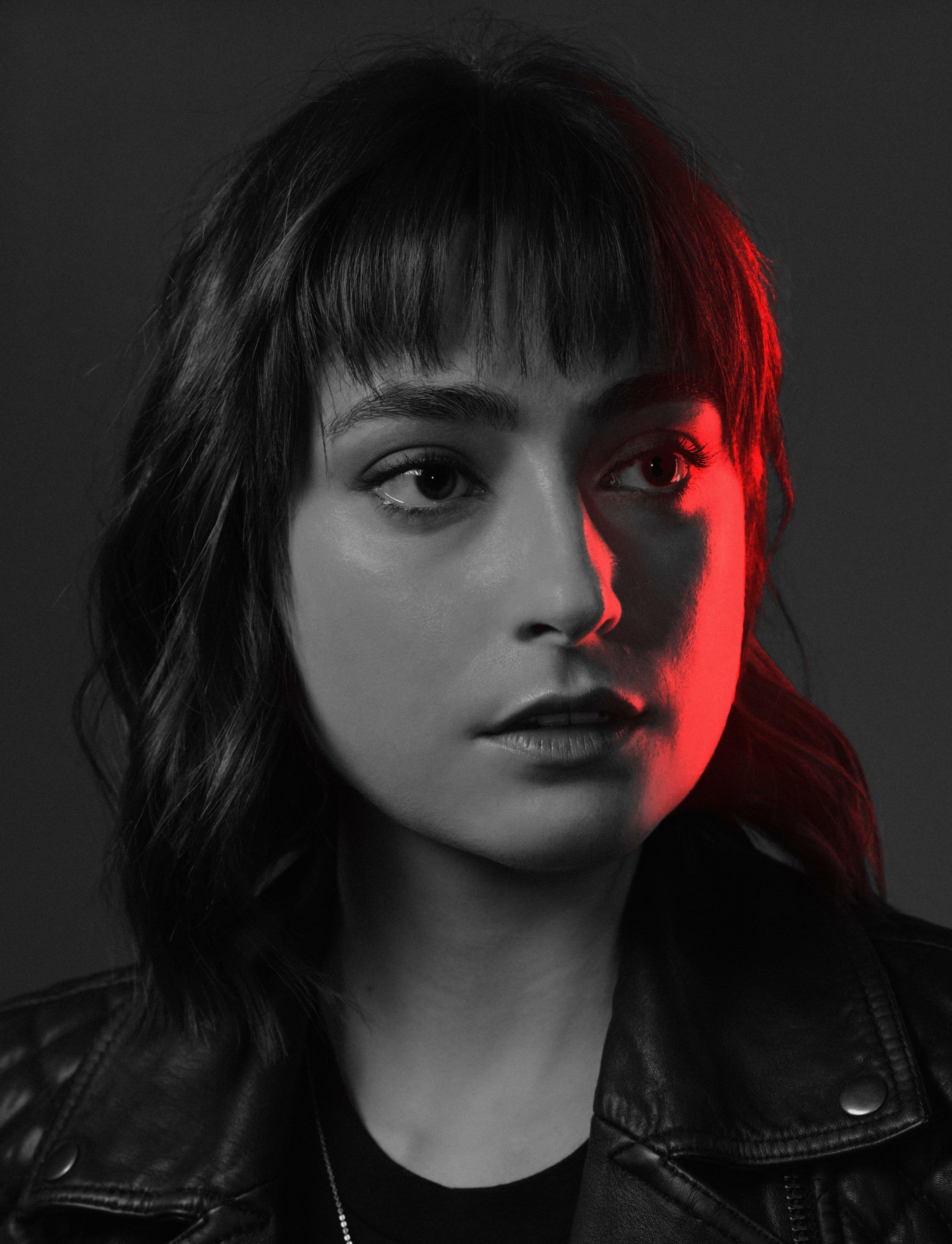 black and white photo of a young actor in a black leather jacket looks at us. half of her face is illuminated in red.