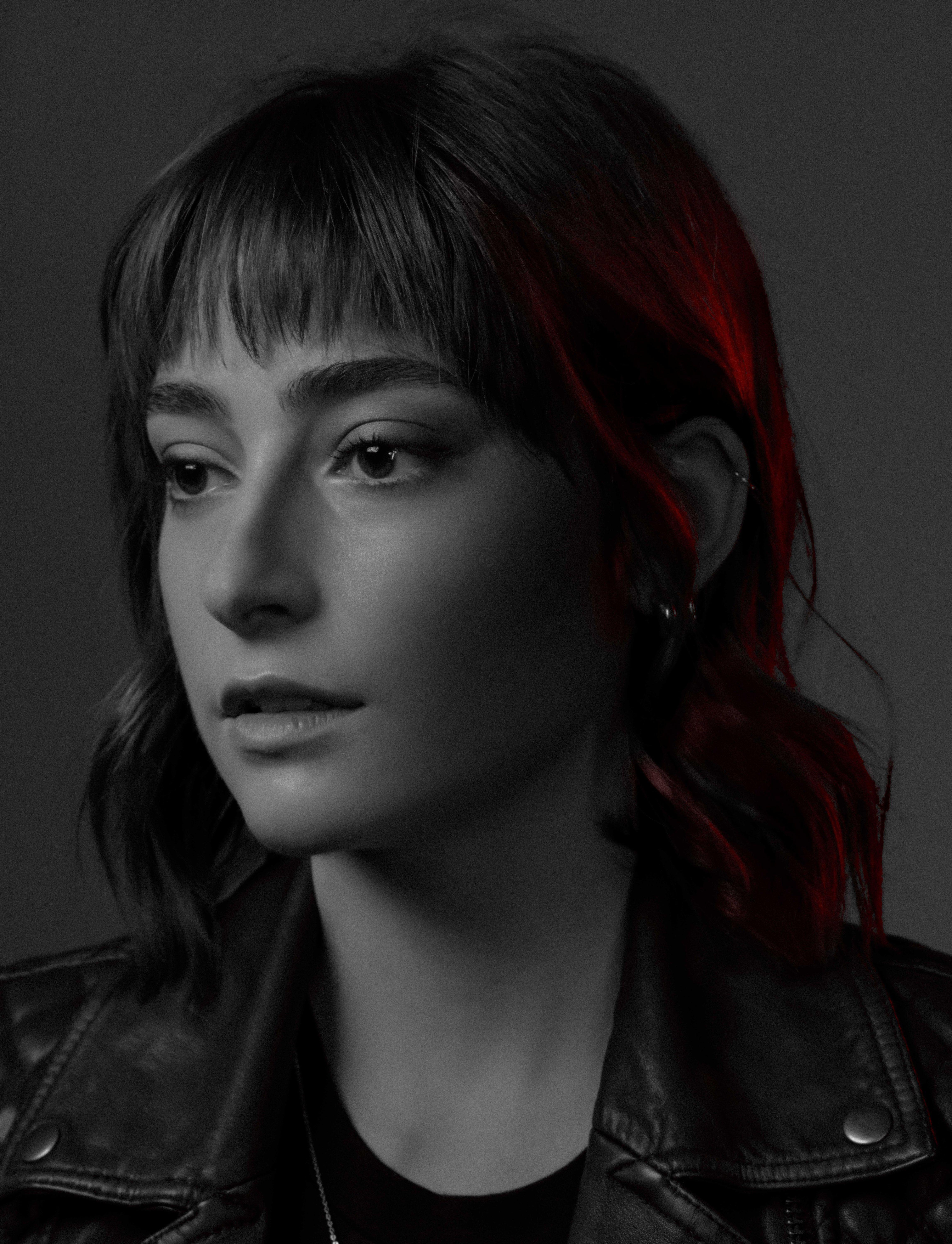 black and white photo of a young actor in a black leather jacket looks at us. half of her face is illuminated in red.