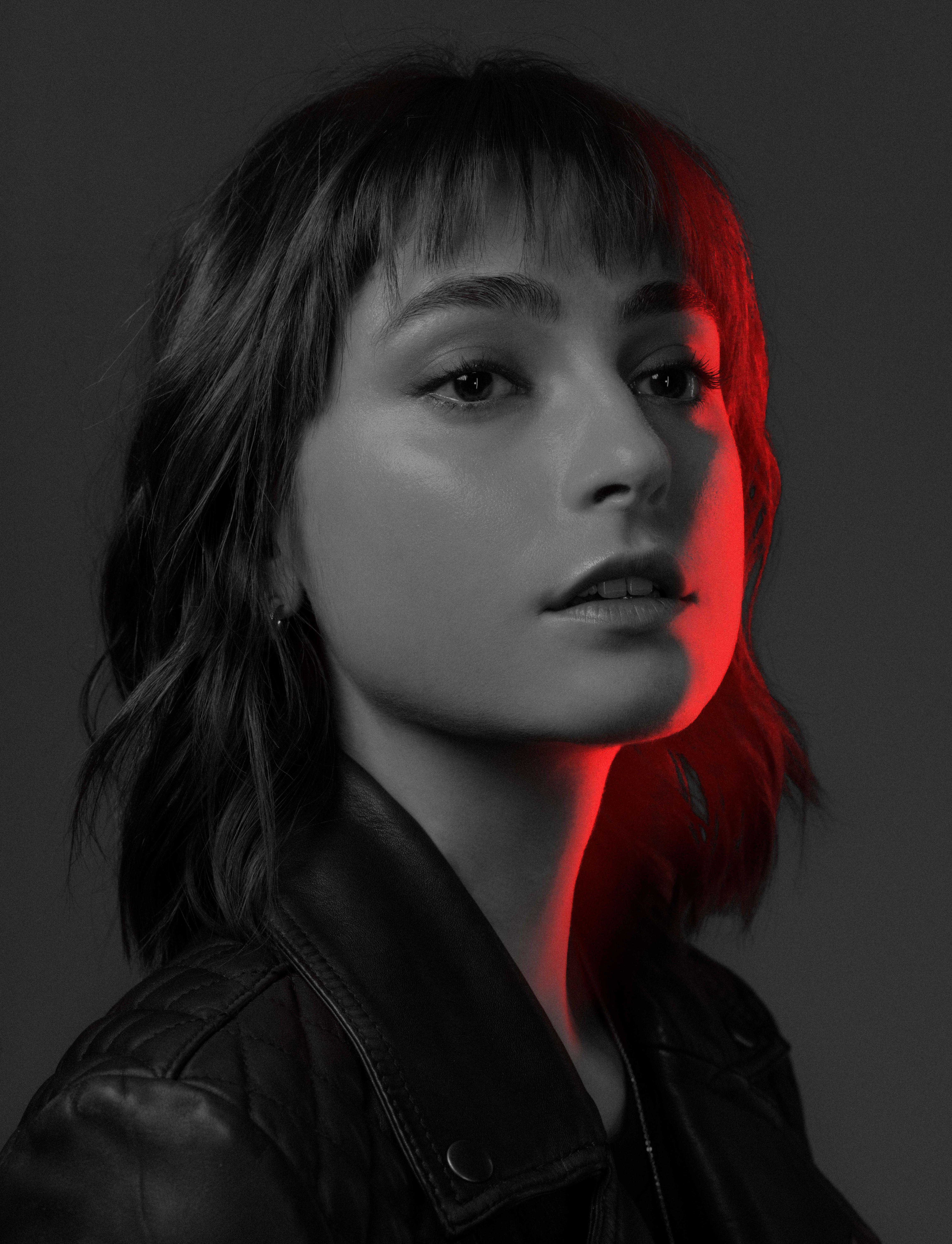 black and white photo of a young actor in a black leather jacket looks at us. half of her face is illuminated in red.